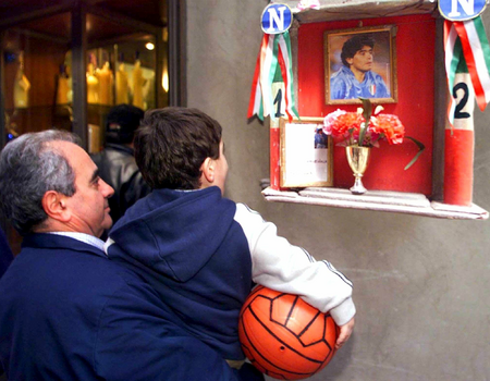 Een inwoner van Napels bidt met zijn kleinzoon voor de gezondheid van de Argentijnse voetballegende Diego Armando Maradona bij zijn altaar. Maradona speelt eind jaren tachtig voor Napoli en leidt het team naar de landstitel en de UEFA Cup. PHOTO/ANSA/Ciro