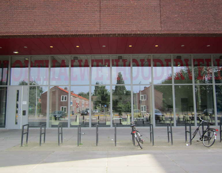 Met grote letters staat  er op het raam: Sporthal Wethouder Verhey. In het raam weerspiegelen zich de huizen van Tuinwyck.