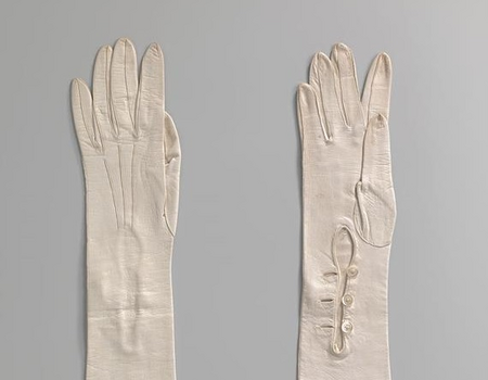 Paar lange dameshandschoenen van wit glacéleer. Op de hand drie stiksels. Bij de pols sluitend middels drie witte kunststof knopen. Amsterdam Museum (objectnummer KA 17210).